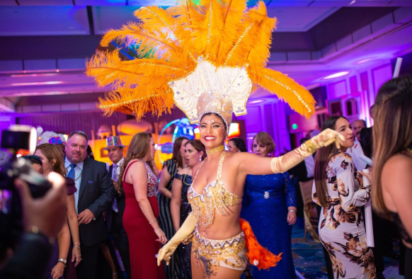 Masked performer in orange feathered costume at a lively indoor party