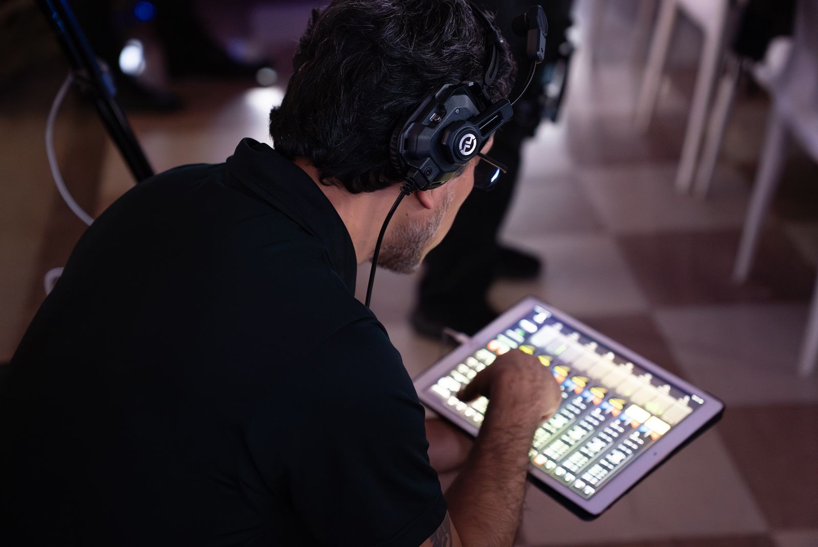 Person wearing headphones uses a tablet with a lit control interface in a dim room