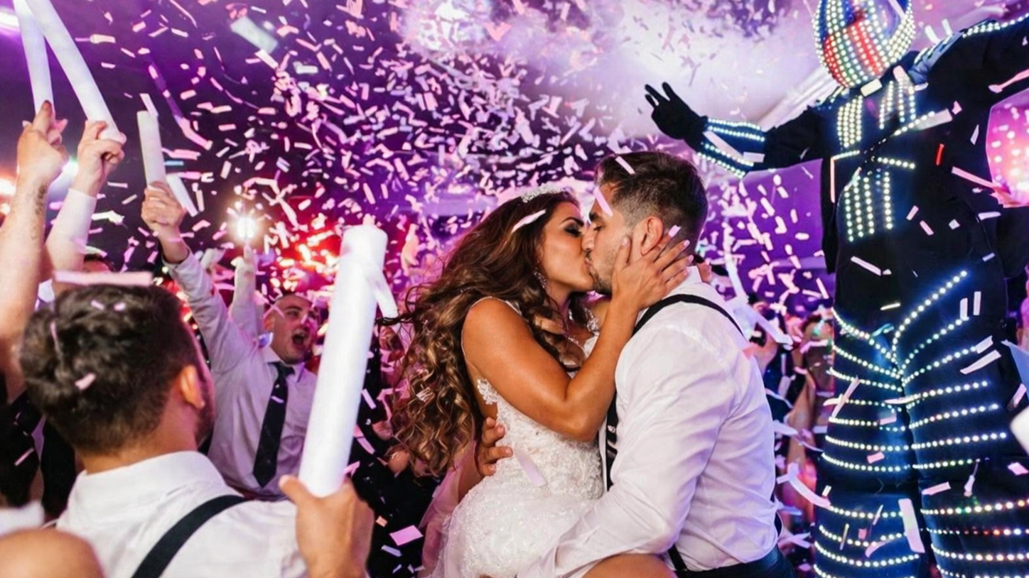 Wedding couple kissing amid confetti and cheering guests at a lively celebration