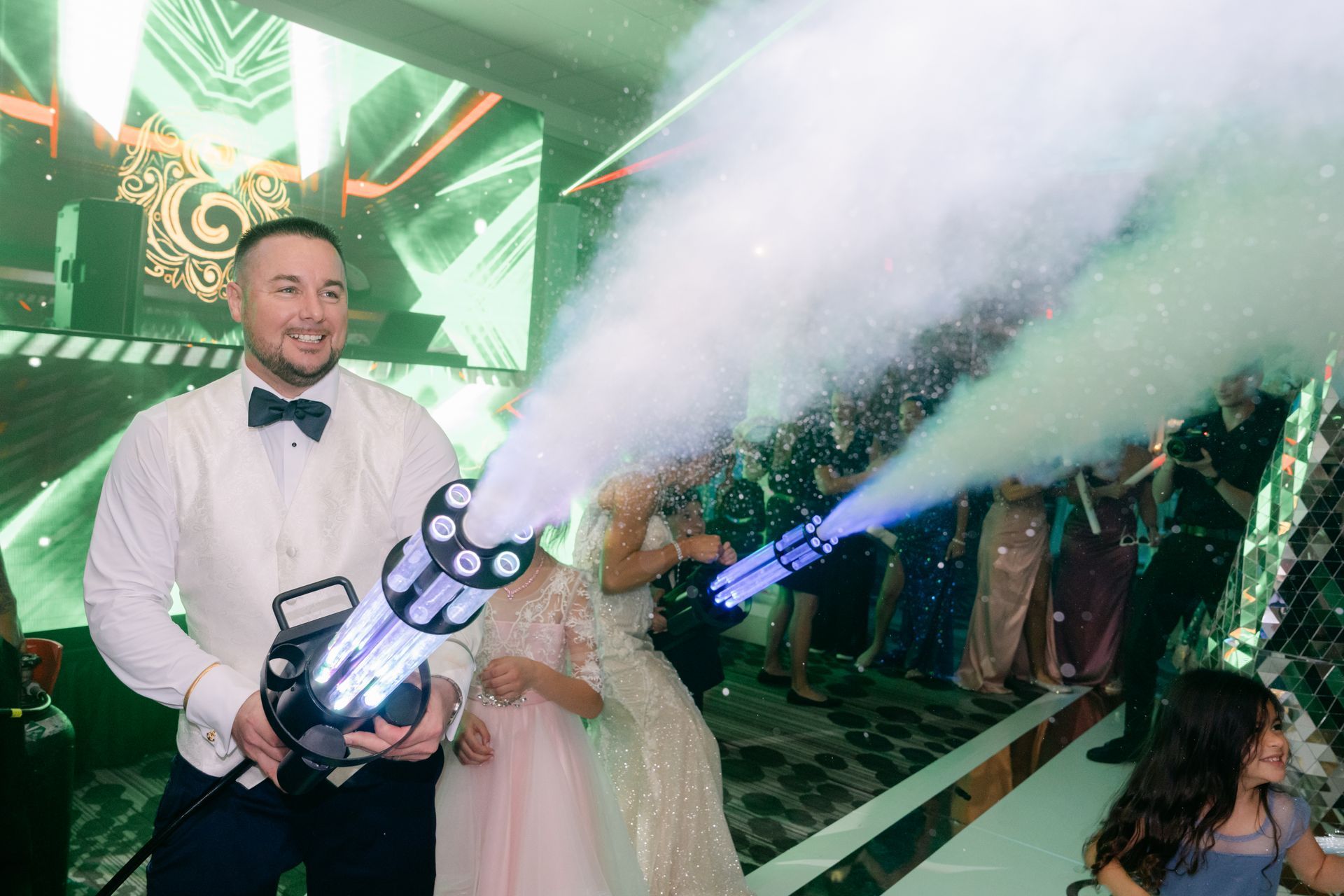 Man in white shirt operates a fog cannon at a lively indoor event with green lighting