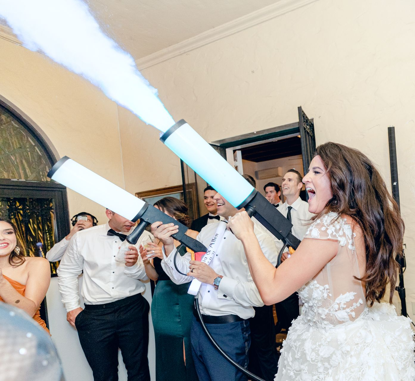 Bride and guests firing white confetti cannons indoors during a wedding celebration