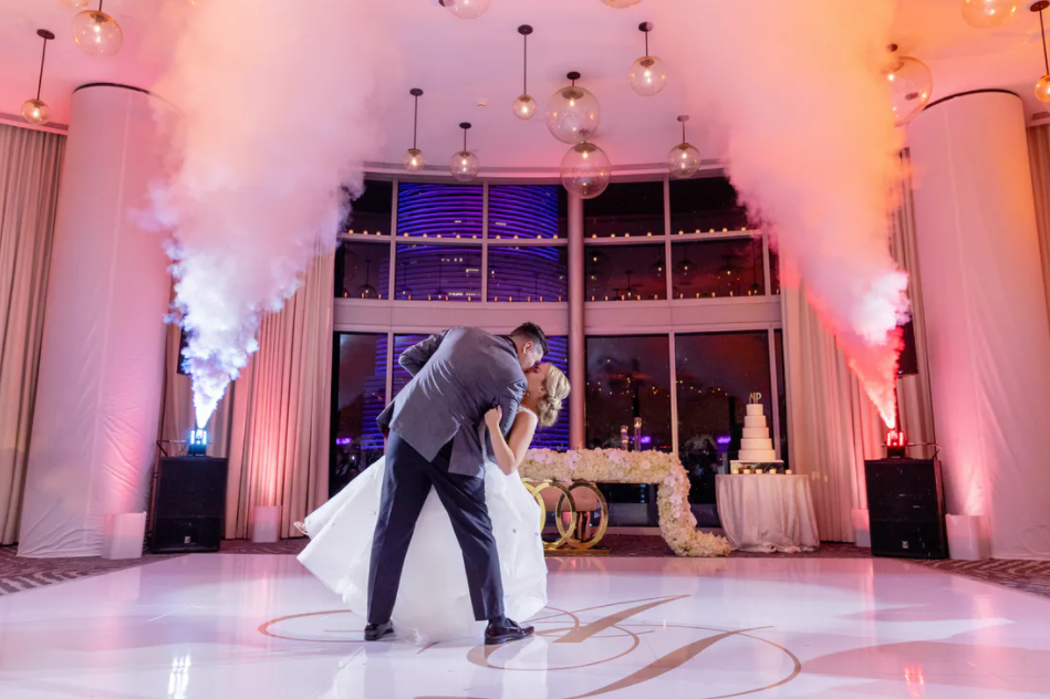 Wedding couple kissing on a ballroom dance floor with pink uplighting and white smoke columns