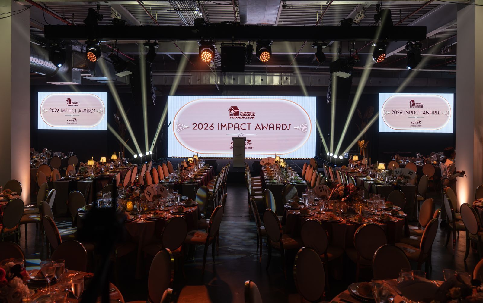 Conference banquet hall with stage and screens, lit by spotlights during an awards ceremony