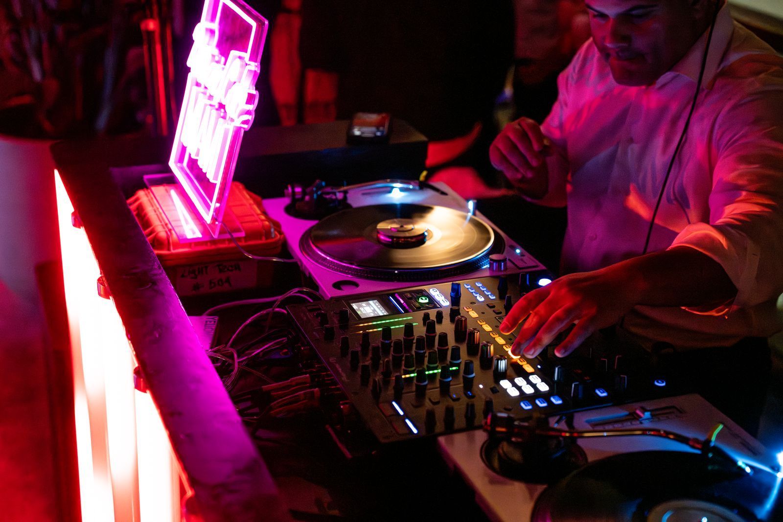 DJ mixing music on turntables and mixer in a neon-lit club, with a glowing laptop nearby