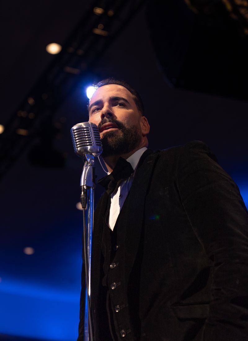 Singer in a dark suit performing into a vintage microphone under blue stage lights