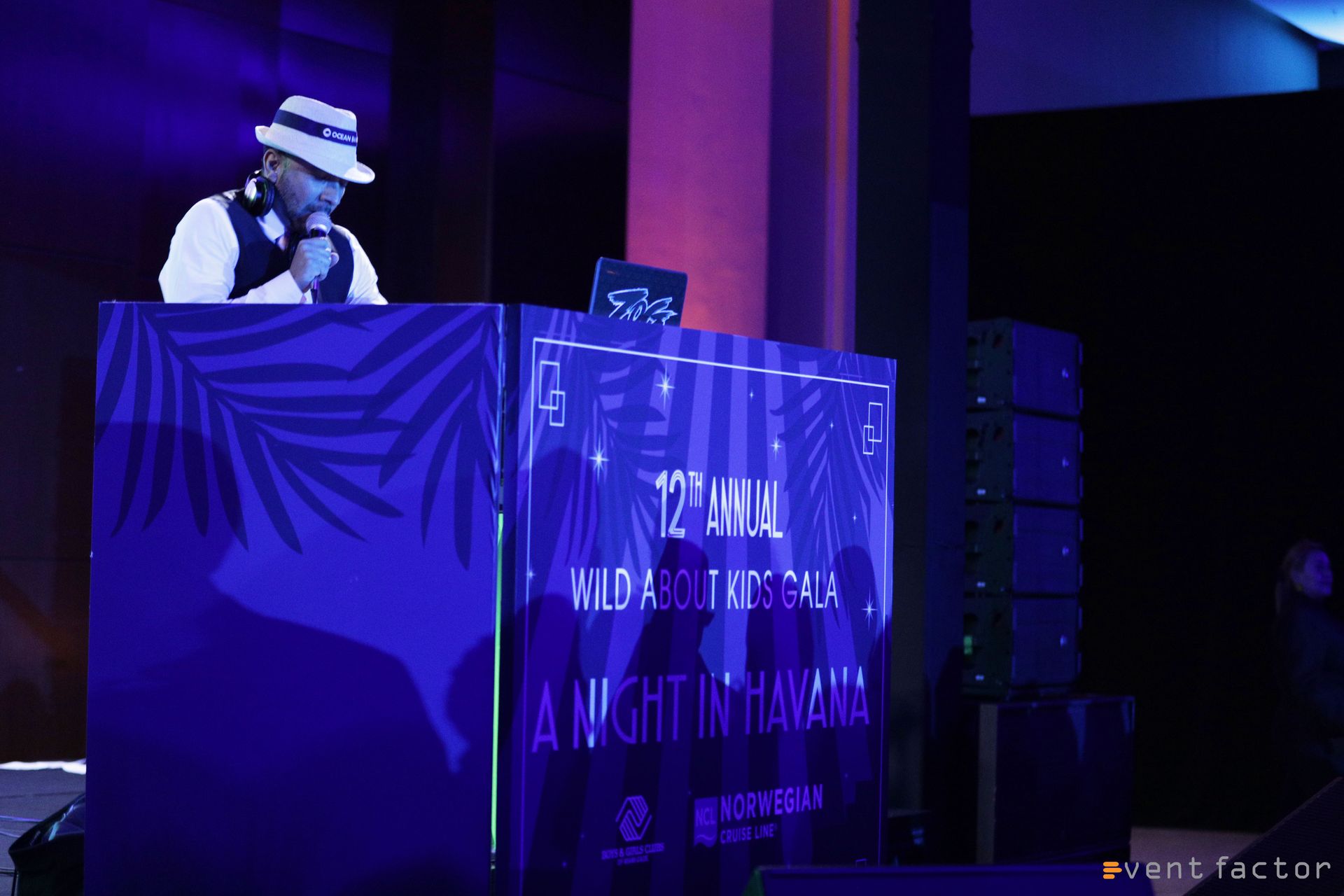 DJ in hat performing behind a blue-lit booth on a stage with purple lighting