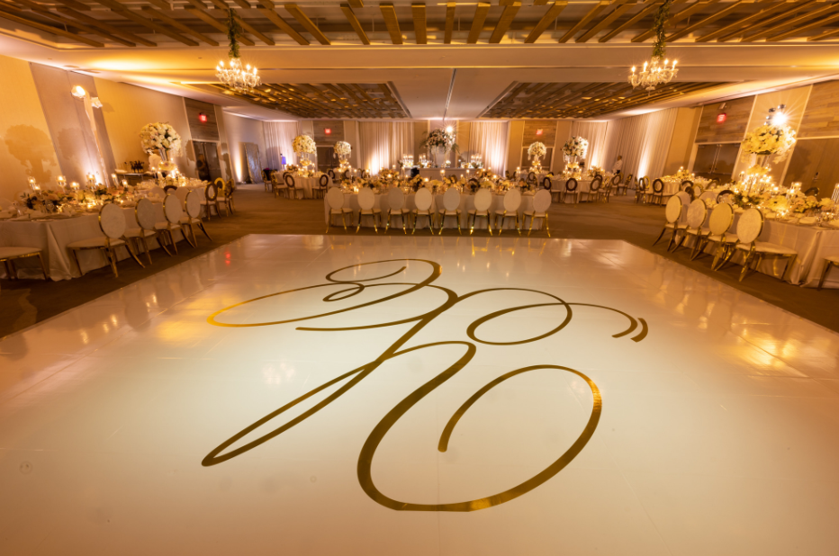 Elegant gold-lit wedding reception hall with round tables and a glossy dance floor monogrammed with “30”