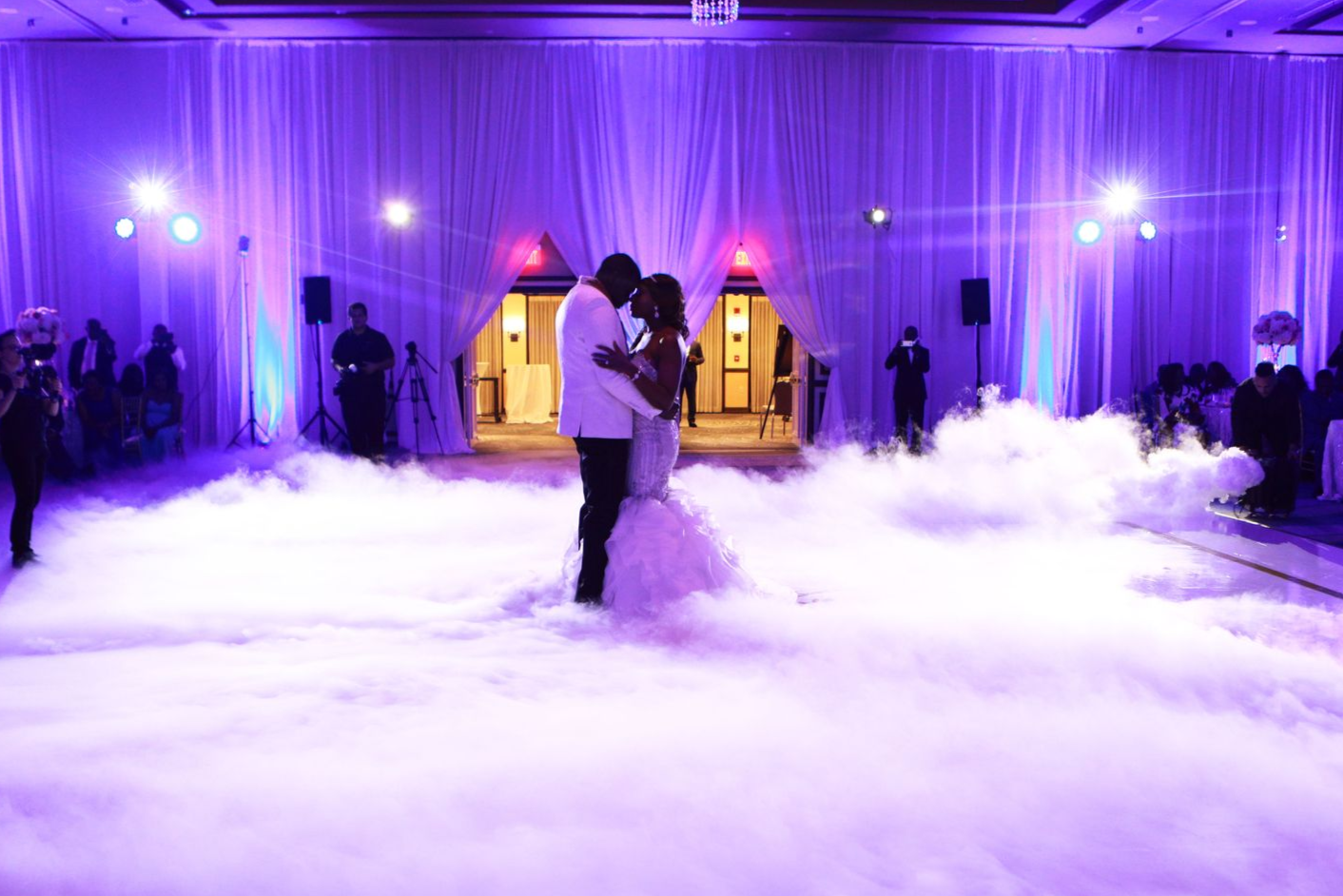 Couple dancing amid purple-lit fog on a wedding reception floor