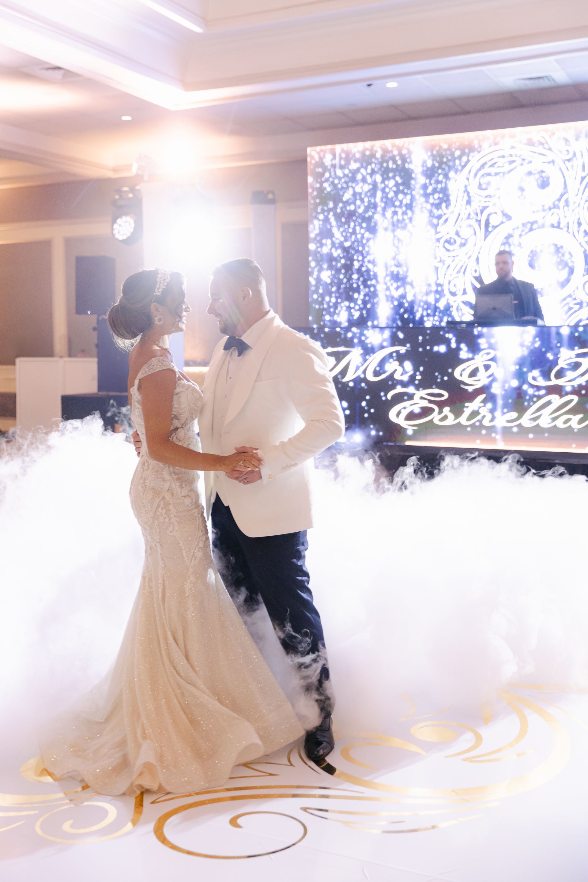 Bride and groom slow dance in a fog-filled reception hall with sparkling backdrop