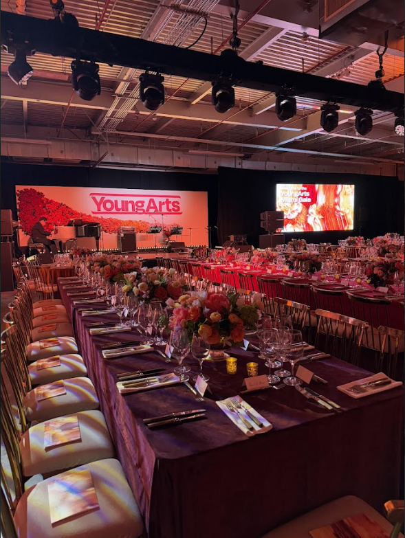 Elegant banquet hall set for a YotepArts event with round tables, floral centerpieces, and a stage with red backdrop.