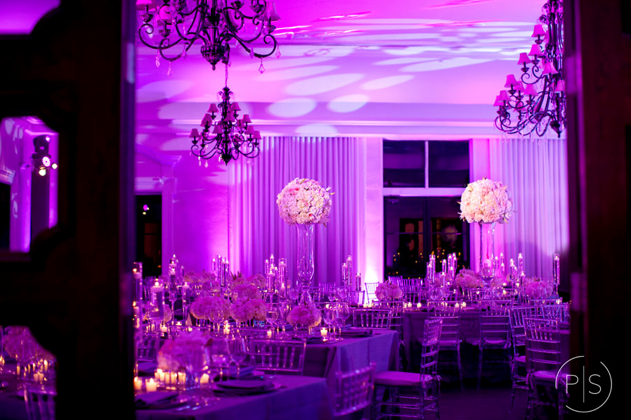 Purple-lit banquet hall with chandeliers, tall tables, and windowed backdrop
