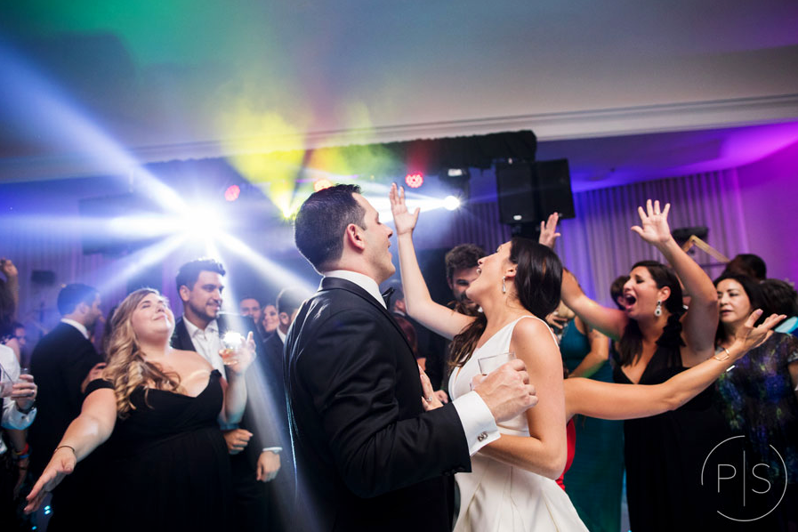 Wedding couple dancing amid cheering guests under colorful party lights