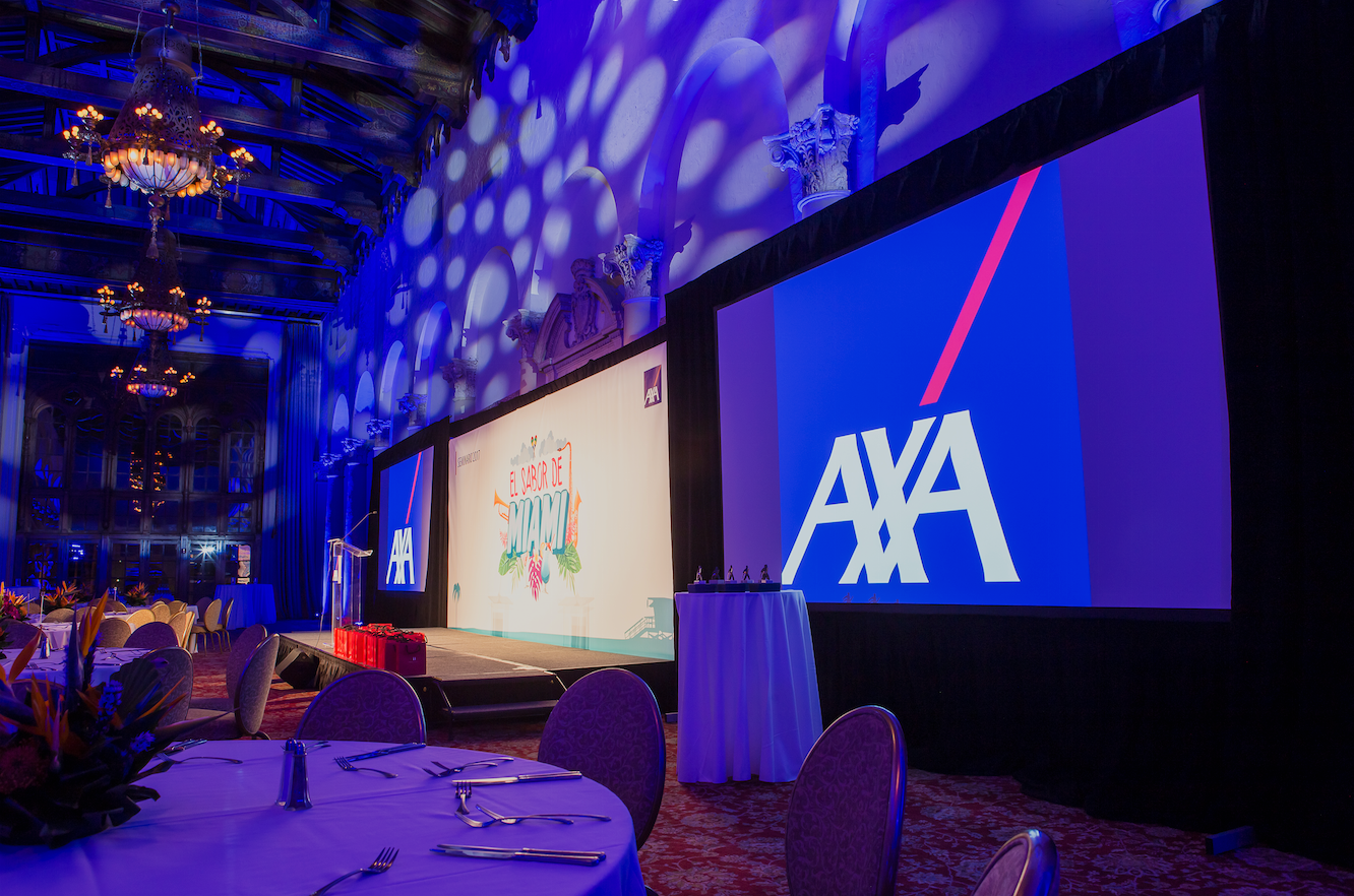 AXA-branded event hall with blue lighting, stage screens, and round banquet tables set in the foreground