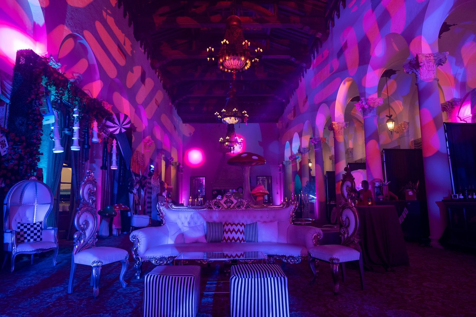 Purple-lit lounge with patterned arches, hanging lanterns, and white couches and tables