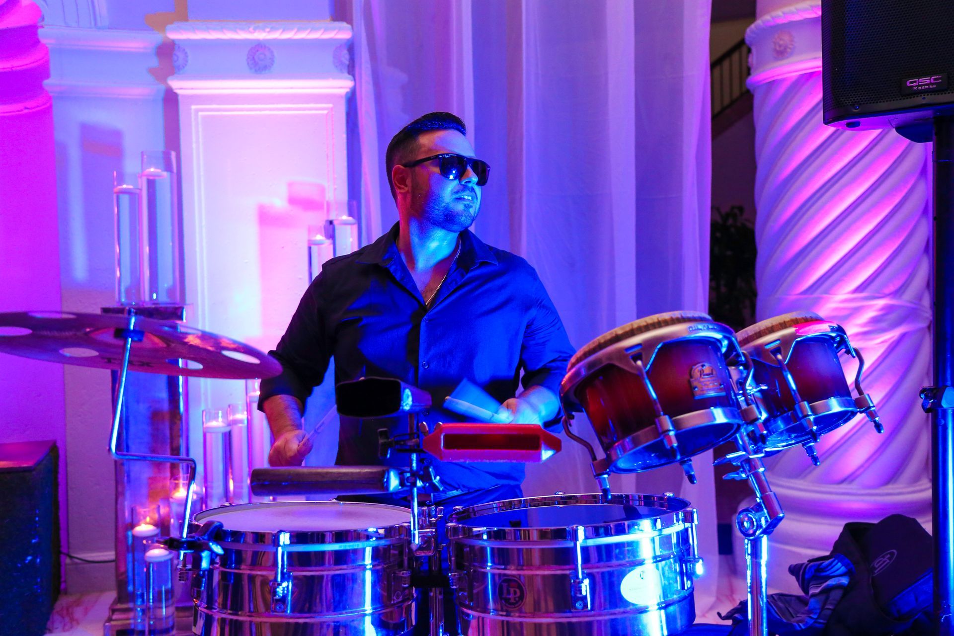 Drummer in sunglasses playing a blue-lit drum kit on stage
