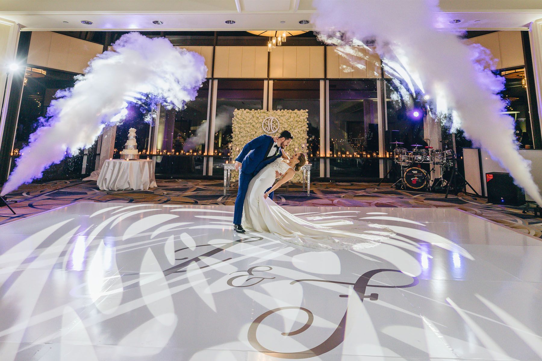 Bride and groom kissing on a lit dance floor with white smoke effects and projected floral patterns