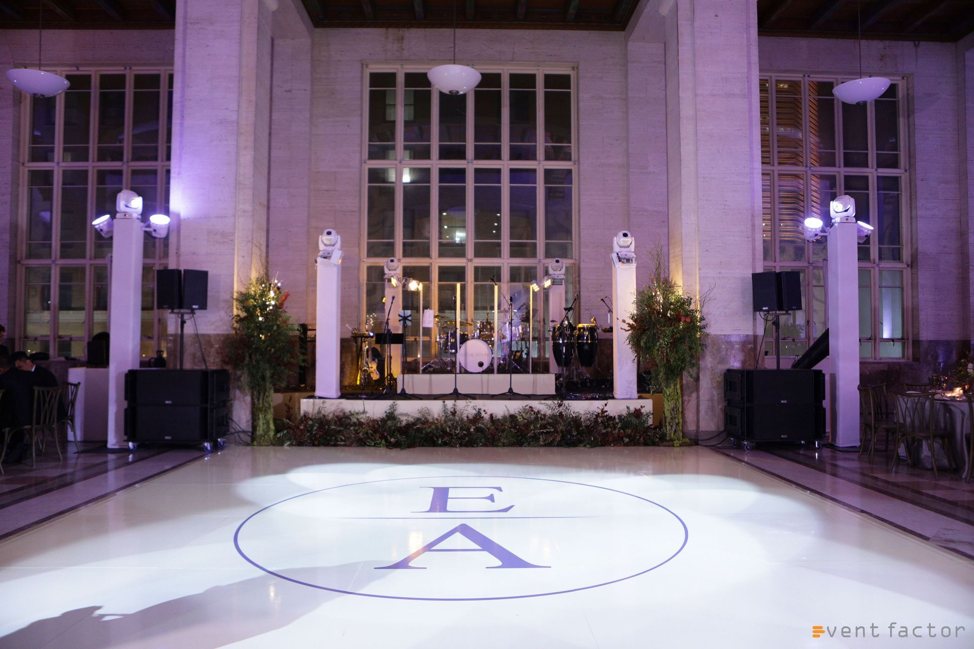 Elegant indoor event space with a lit dance floor and stage in front of tall glass doors and columns
