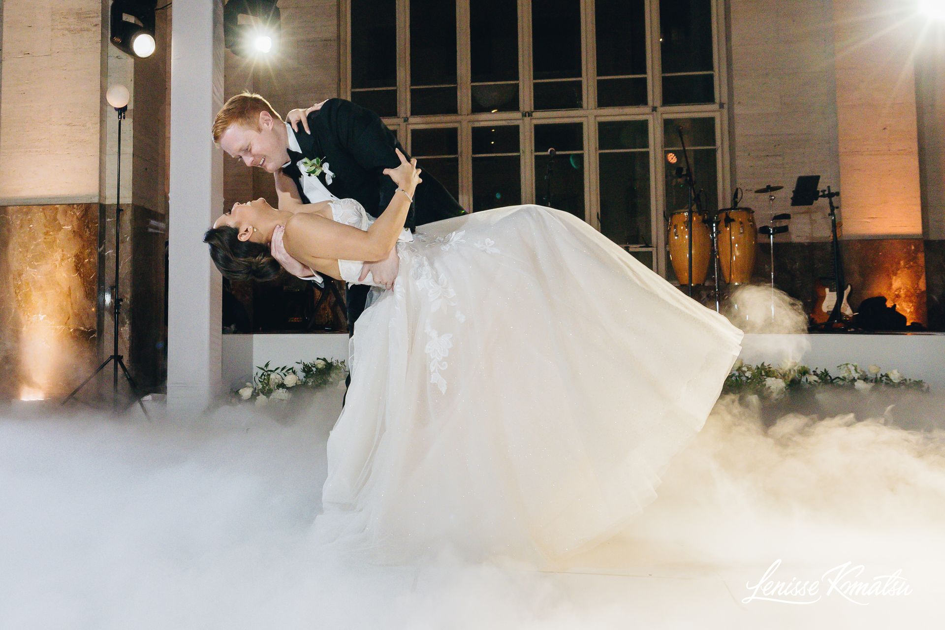 Bride and groom dancing in a fog-filled ballroom, bride in a white gown and groom in a black suit