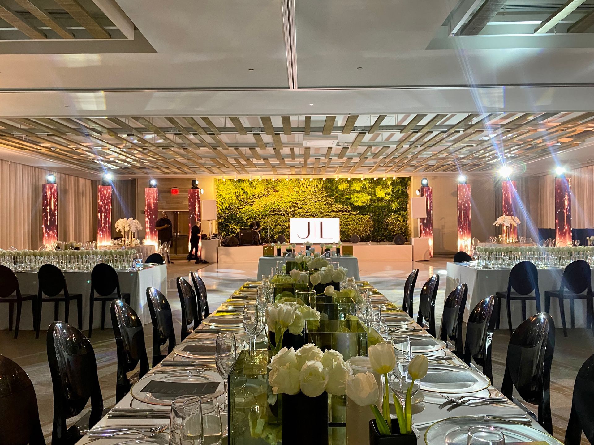 Elegant banquet hall with long decorated tables, white chairs, and a lit floral stage at the far end