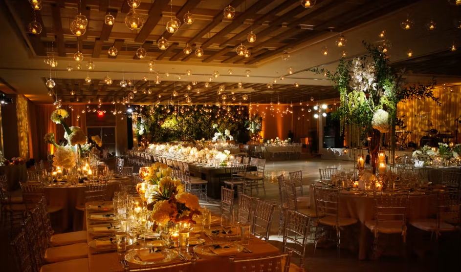 Elegant banquet hall with warm lights, floral centerpieces, and rows of clear chairs set for an event
