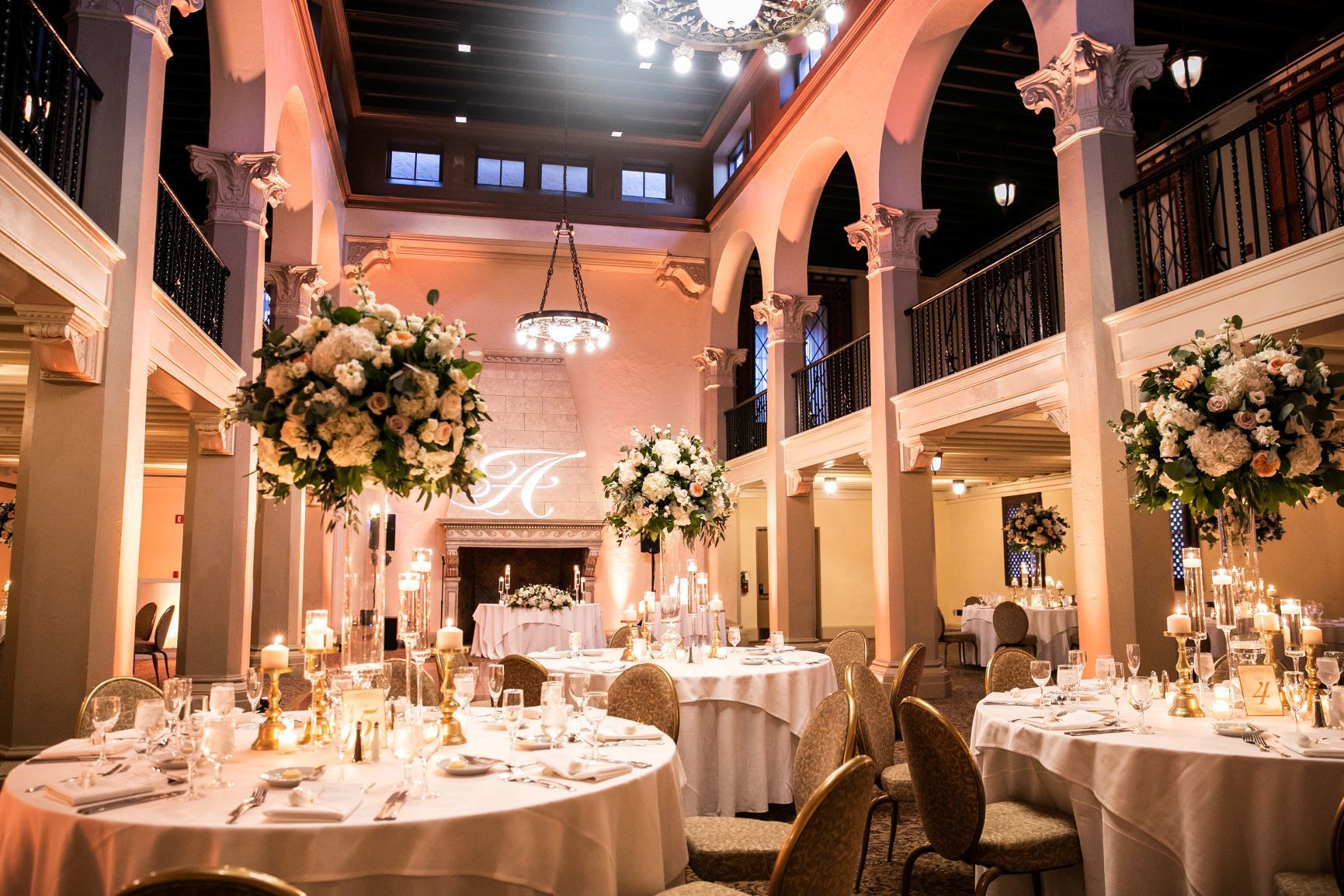 Elegant banquet hall with round tables, floral centerpieces, chandeliers, and warm lighting