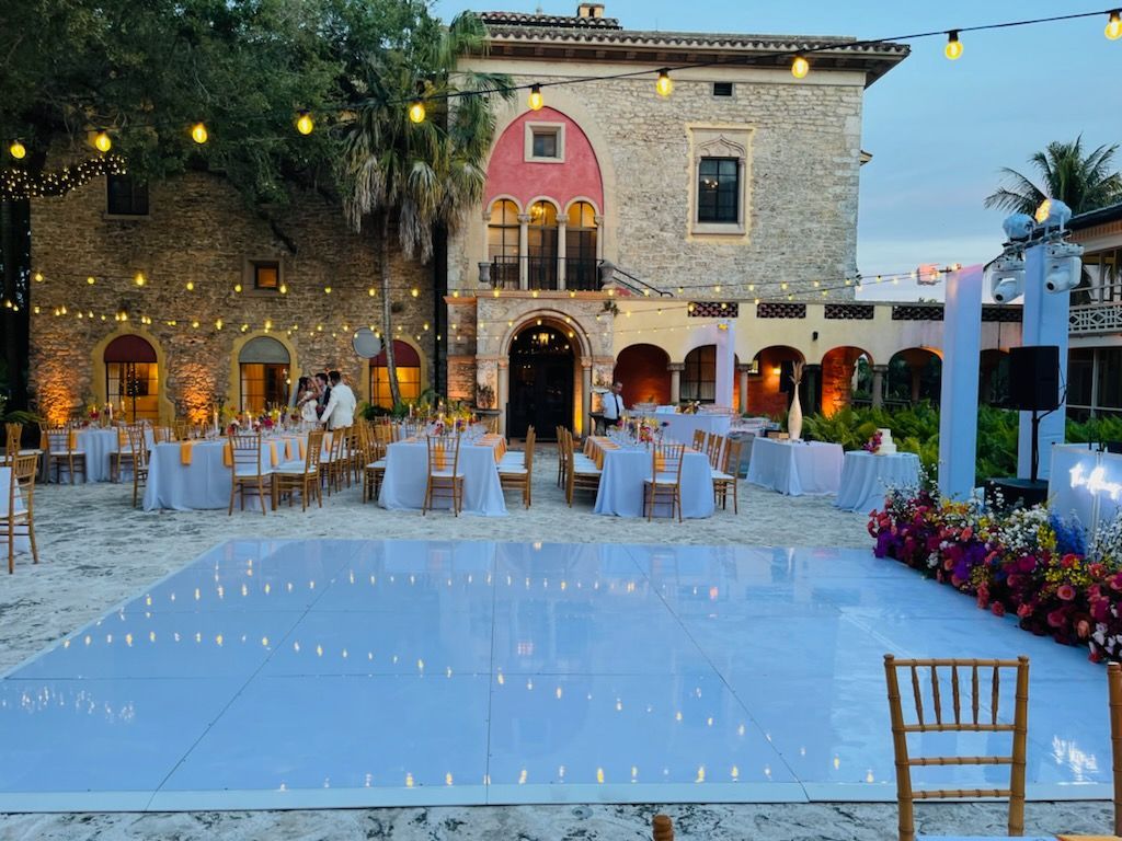 Elegant stone courtyard set for an outdoor evening reception with string lights, tables, and a dance floor