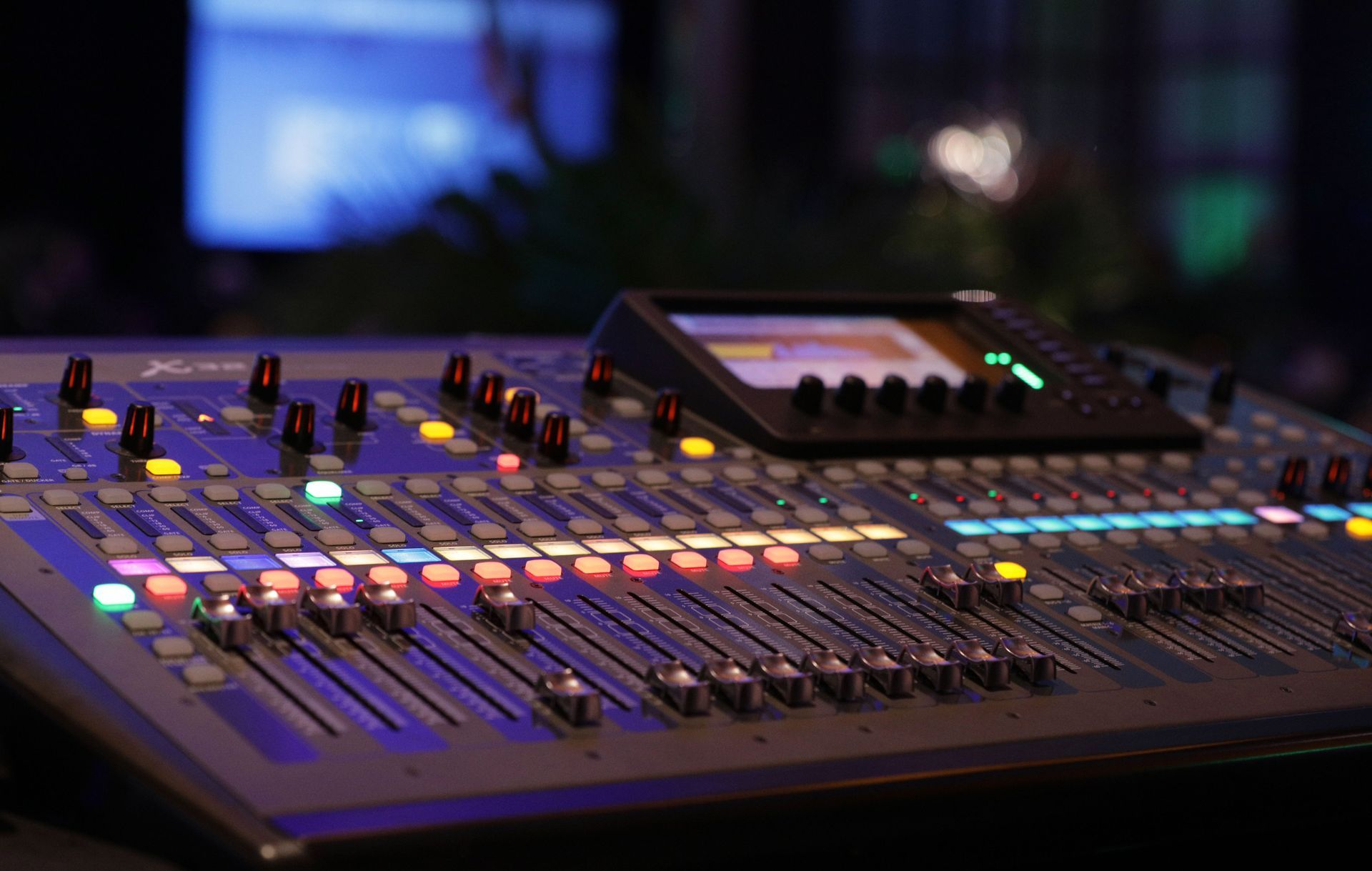 Audio mixing console with illuminated buttons and sliders in a dim studio setting
