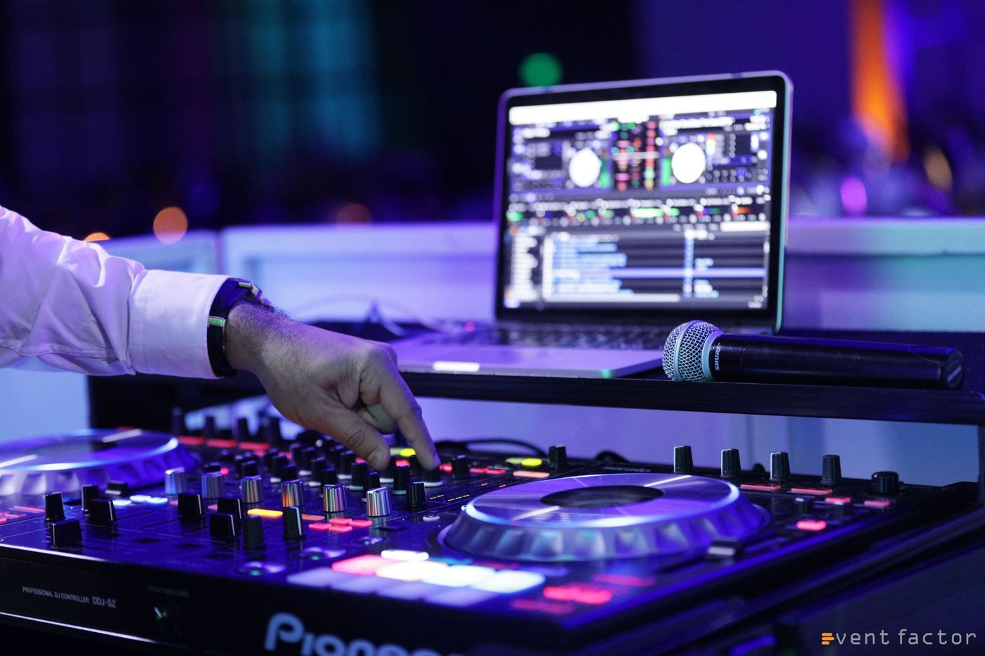 DJ hand adjusting controls on a glowing turntable, with laptop and mixer in a purple-lit club scene
