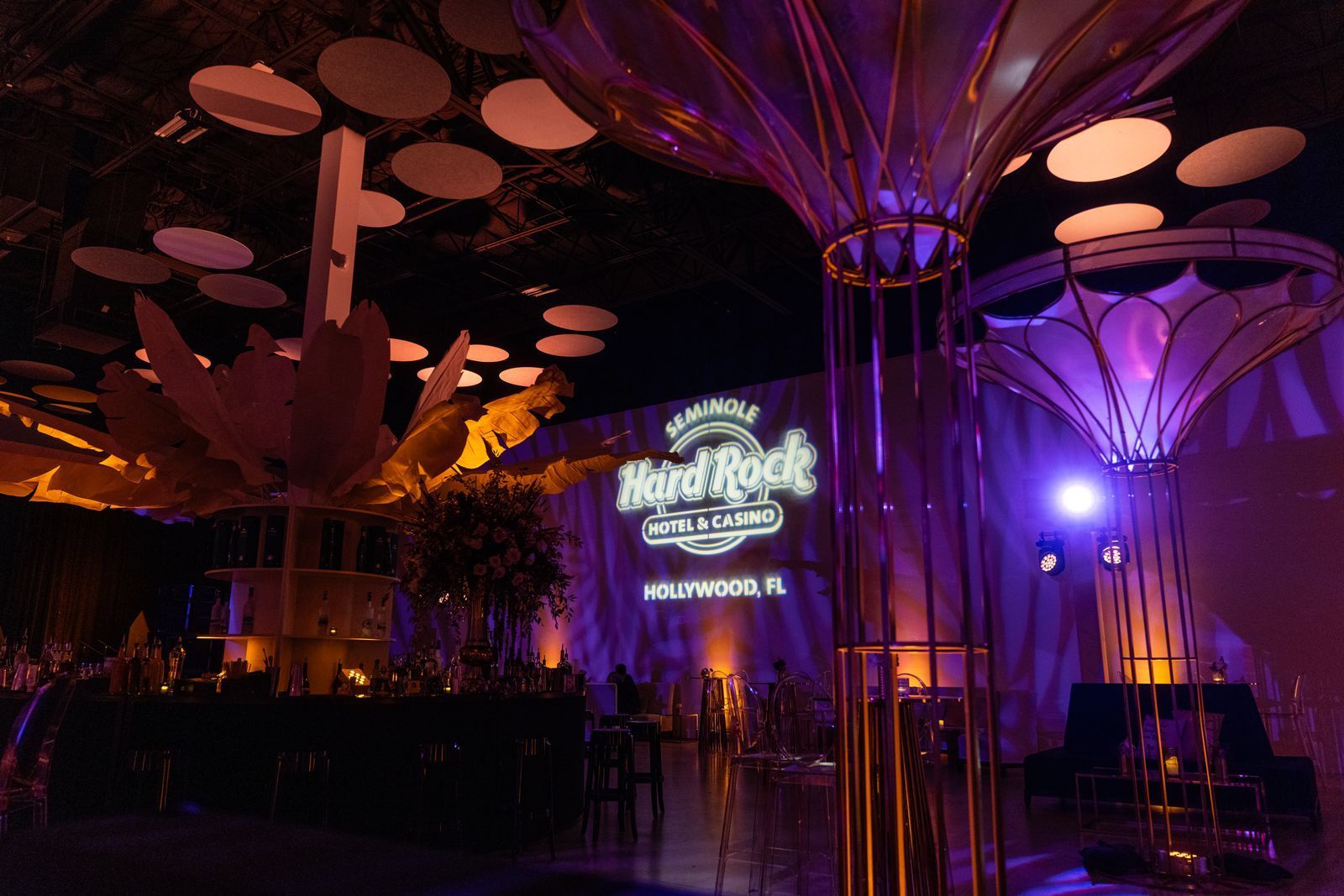 Illuminated event venue with purple and orange lighting, tree-like structures, and a glowing central sign at night