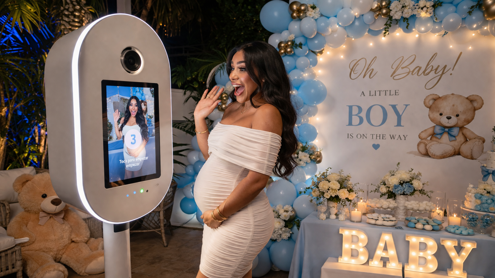 Pregnant woman at blue baby shower beside a baby-themed sign and screen, smiling in an off-shoulder dress