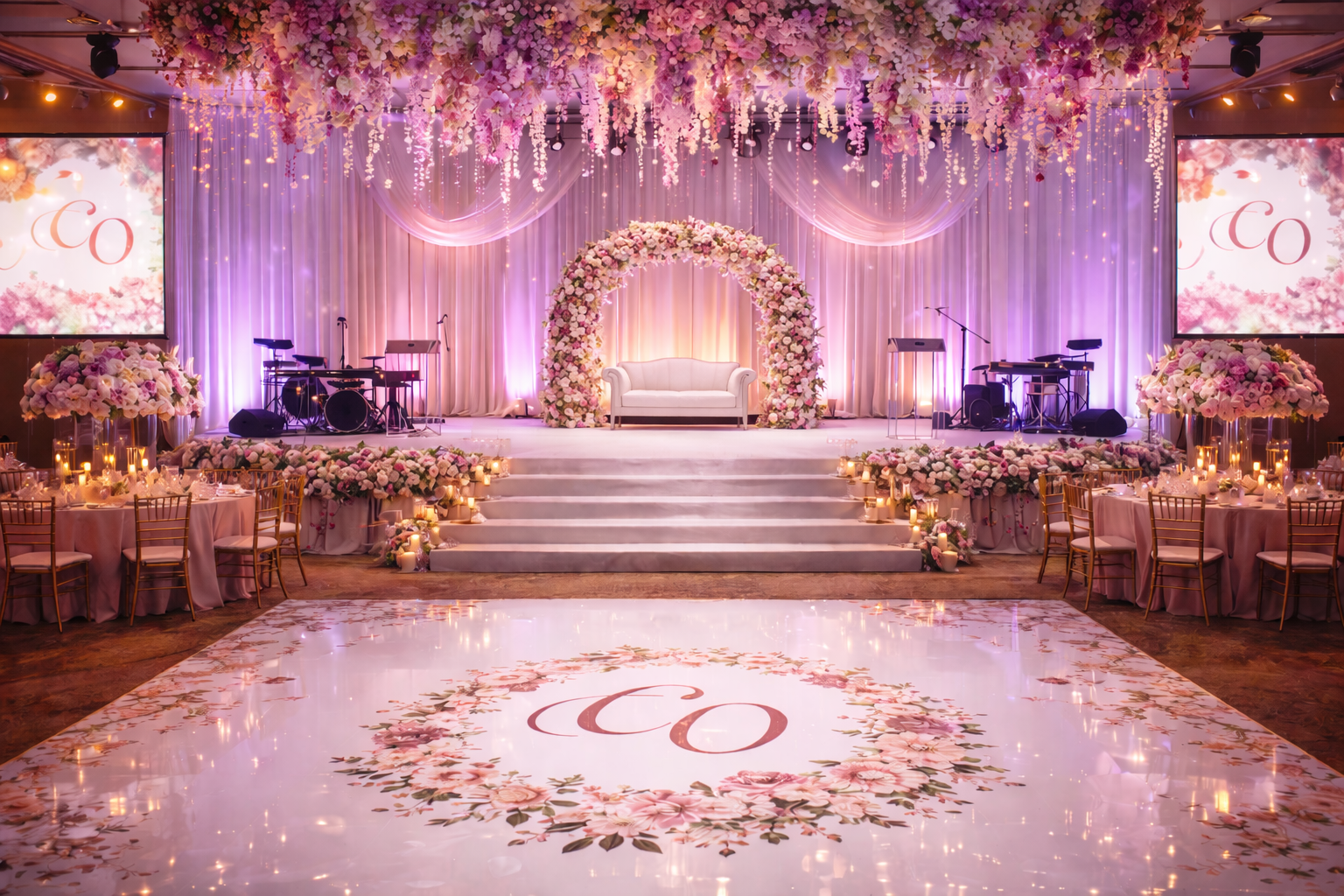 Lavish pink-and-gold wedding stage with floral arch, draped lights, and monogrammed dance floor