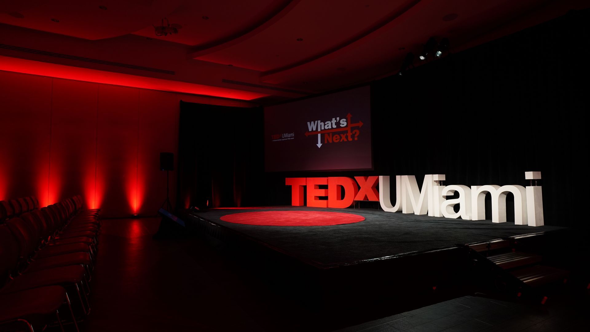 TEDxMiami stage with red lighting and large red-and-white TEDxMiami sign on a dark stage