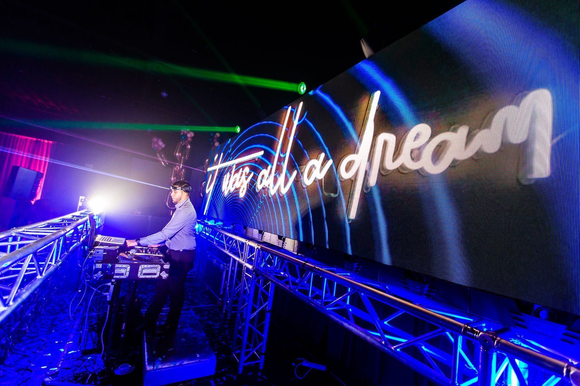 DJ booth under neon lights beside a large “Hall of Dreams” sign