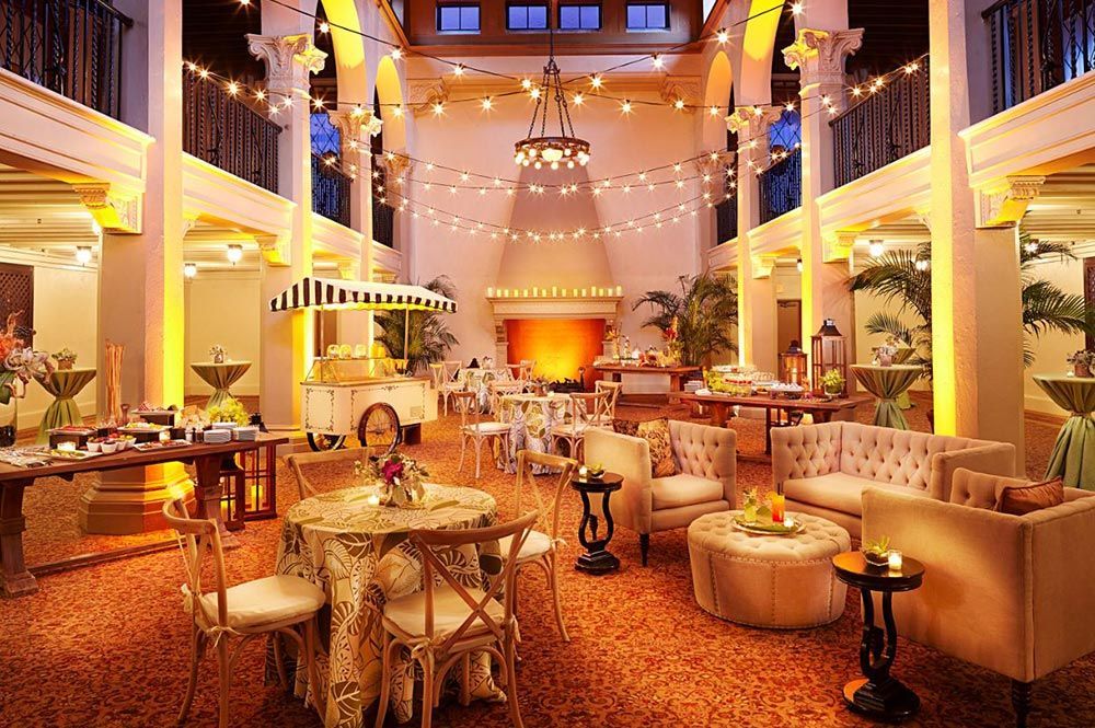 Elegant hotel lobby with warm lighting, chandeliers, plush seating, and tables in a grand atrium