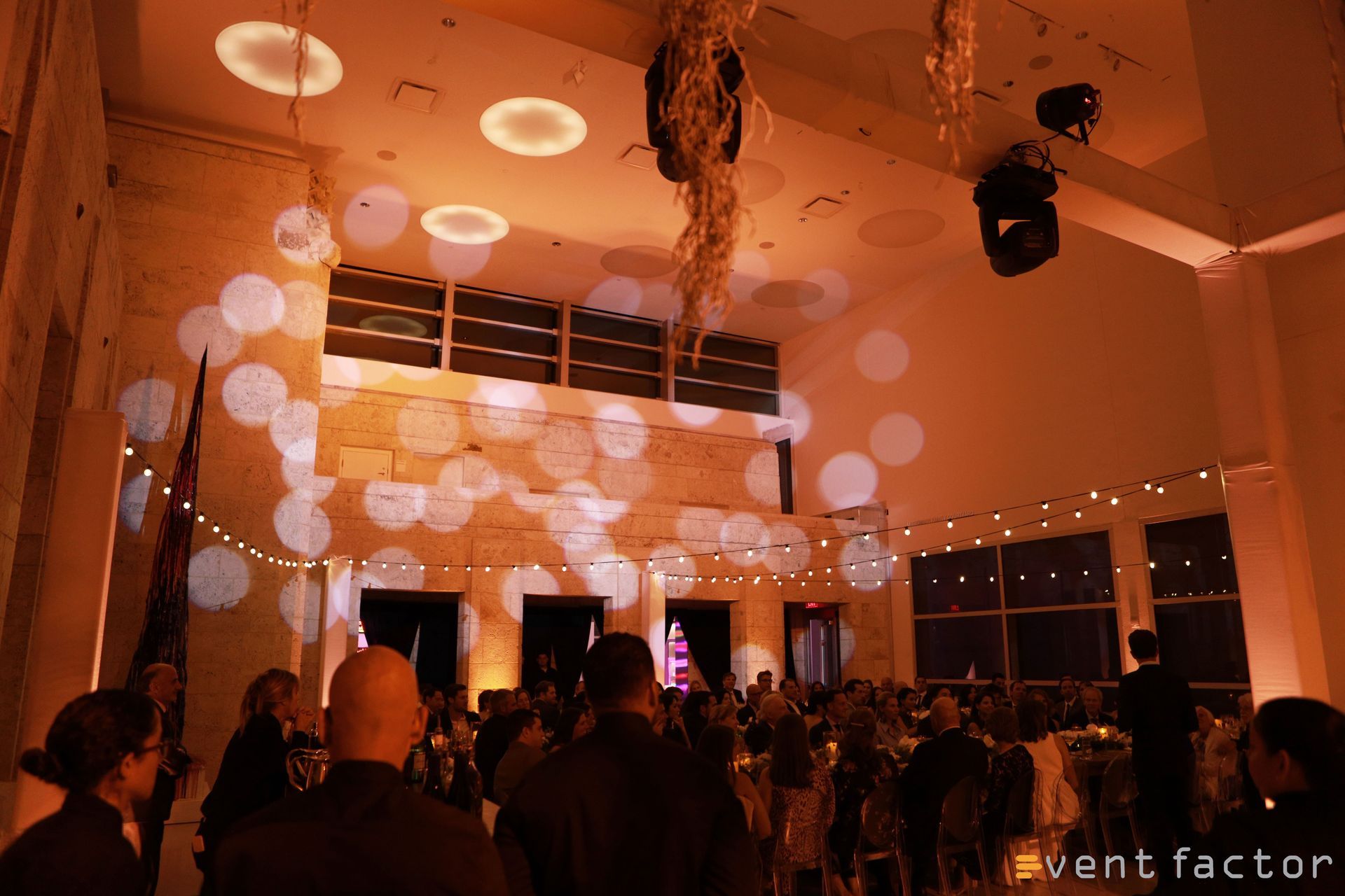 Audience watching a performance under orange lights and white projected circles in a modern event hall