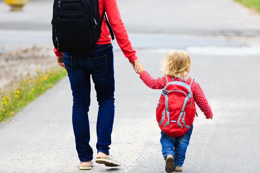 Adult And Child Holding Hands While Walking on a Road, Both Wearing Backpacks and Red Tops — Bowen Childcare & Early Education in Bowen, QLD