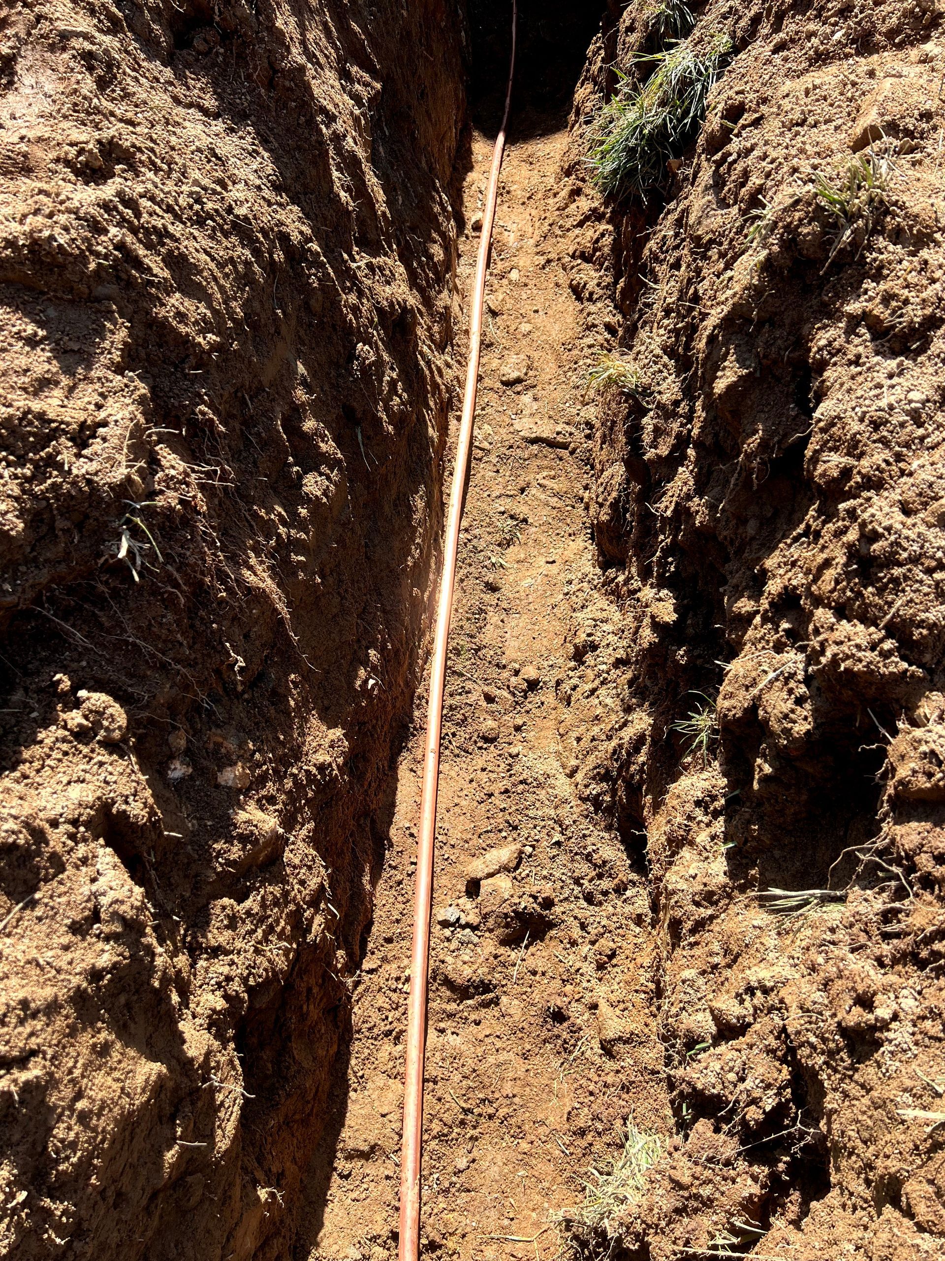 A trench in the ground with a copper wire going through it.