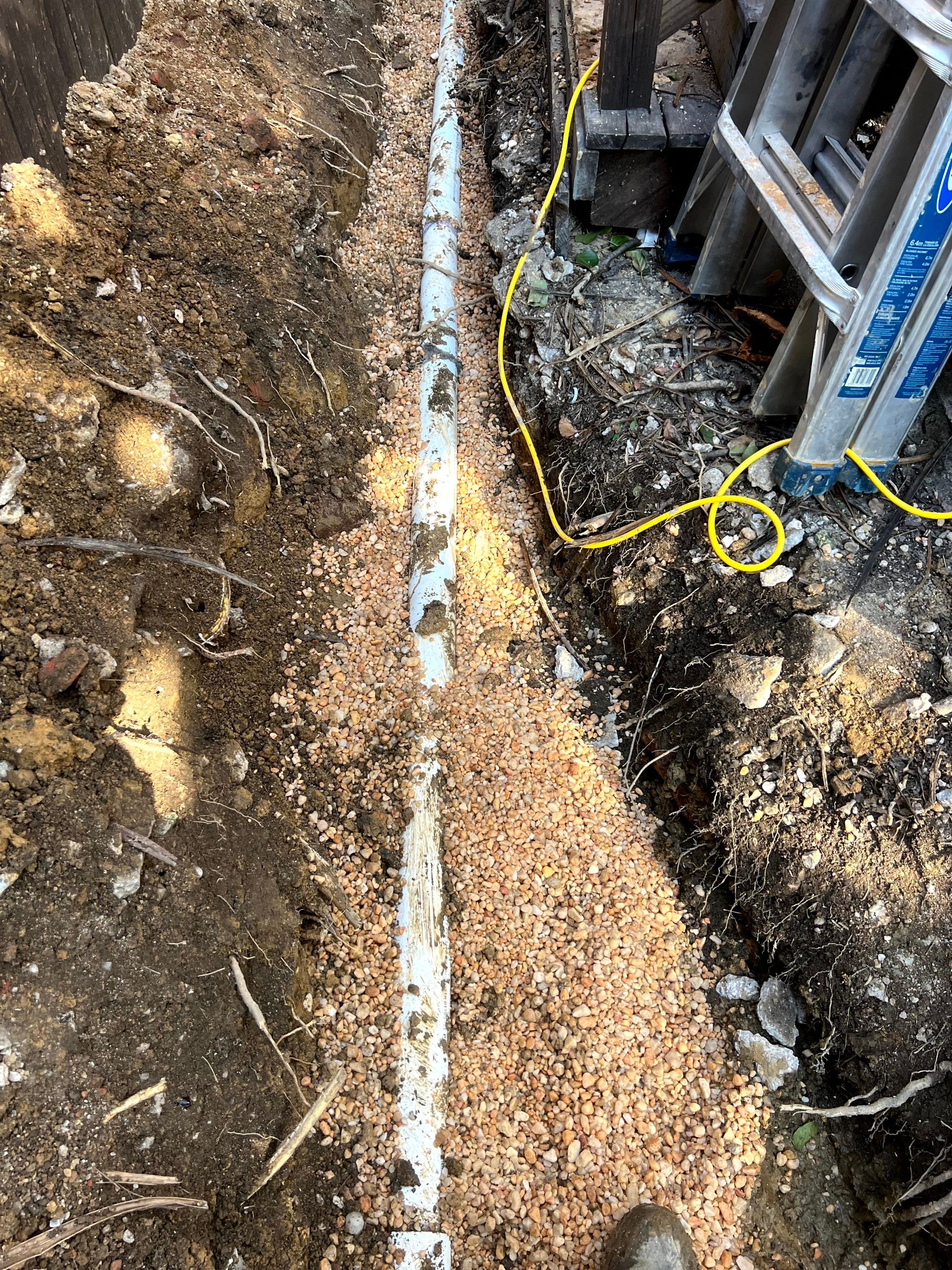 A ladder is sitting in the dirt next to a pipe.