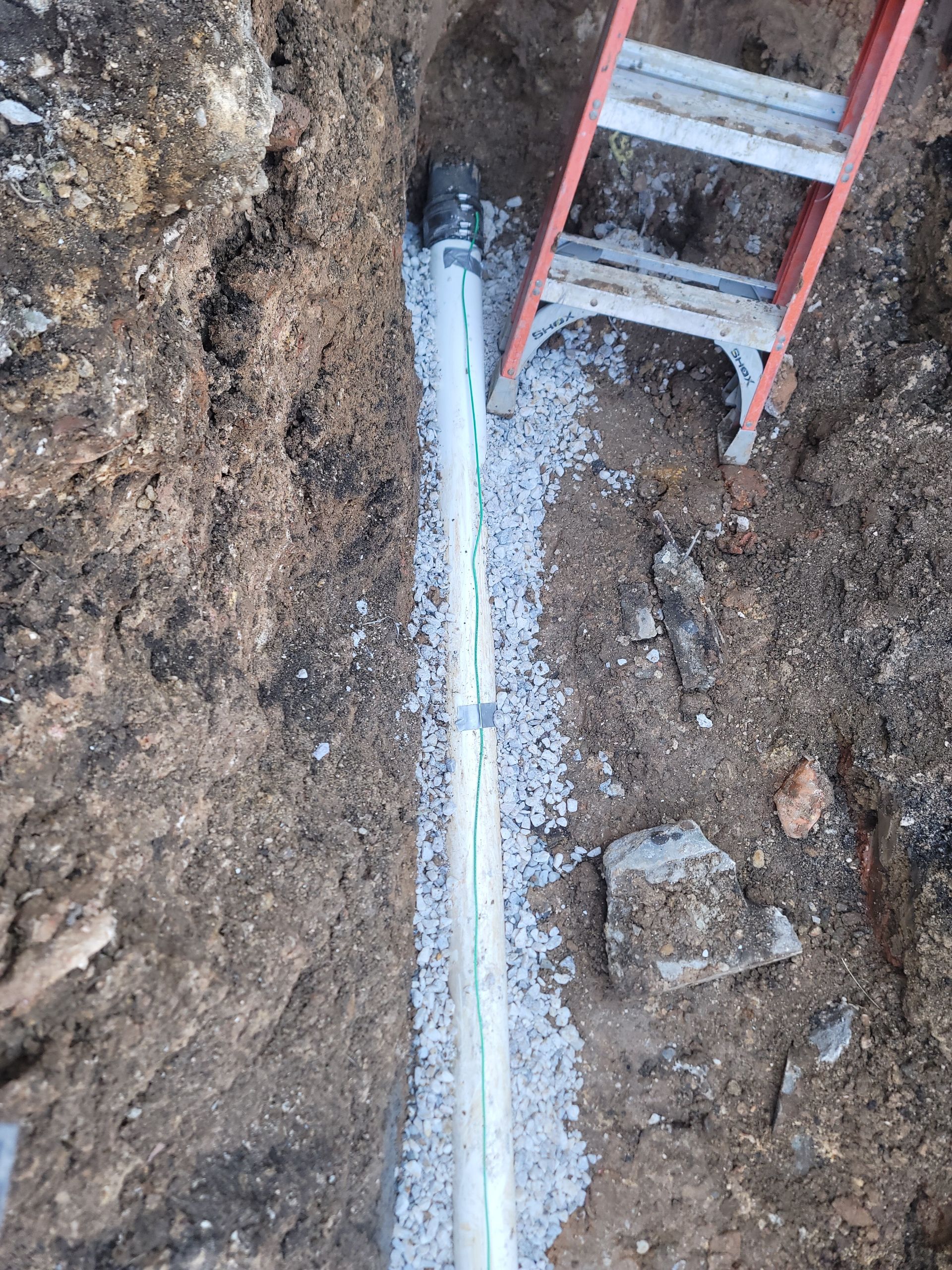 A ladder is sitting next to a pipe in the dirt.