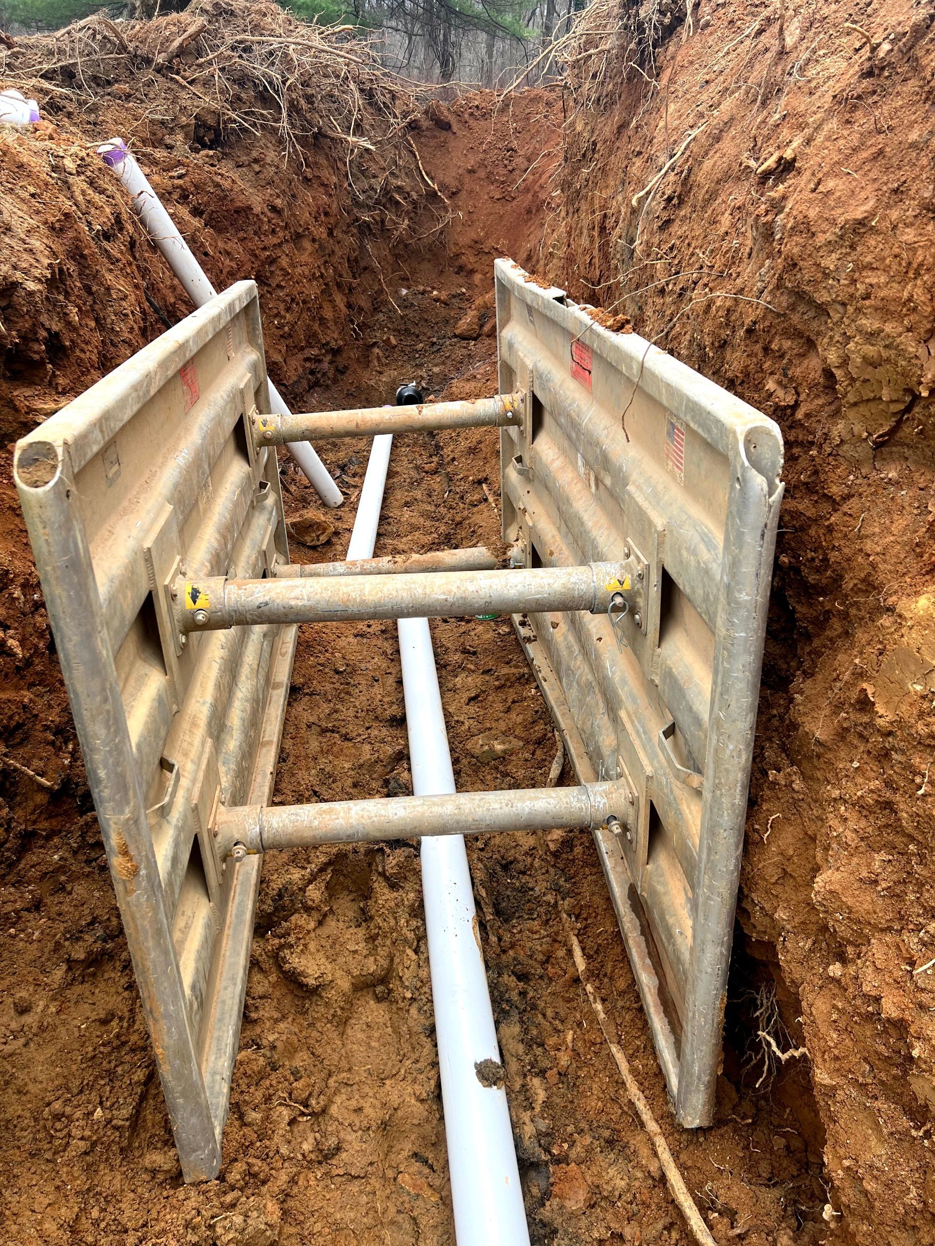 A ladder is sitting in the dirt next to a pipe.