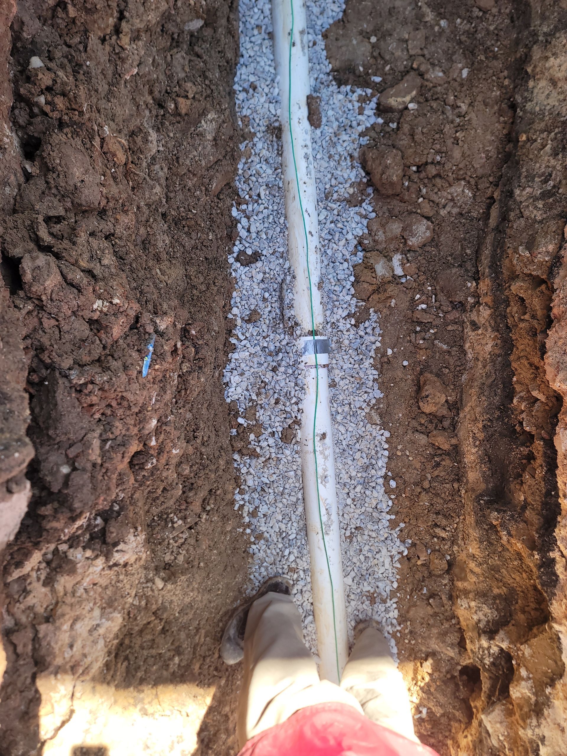A person is digging a hole in the ground to install a pipe.