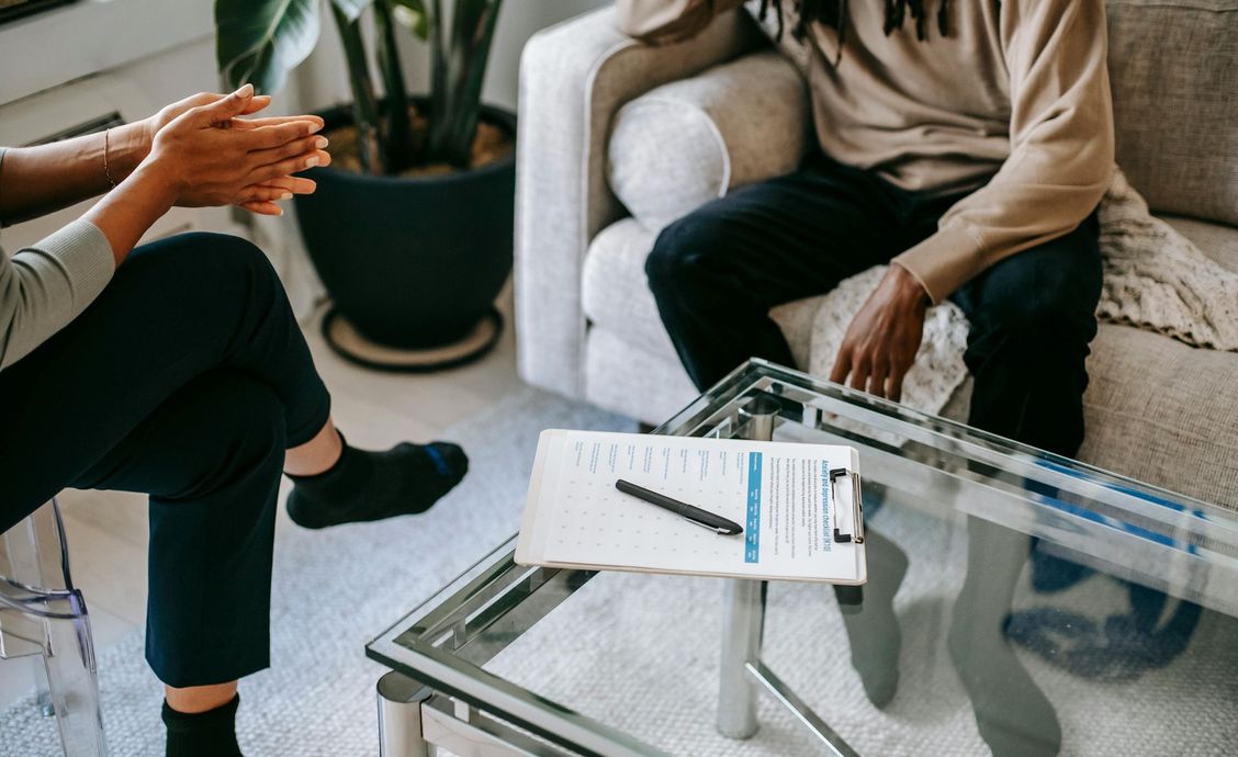 Two people talking beside a glass coffee table with notebooks and a pen in a bright living room