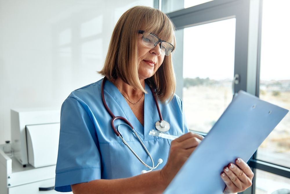 Doctor in blue scrubs writing on a clipboard in a bright office