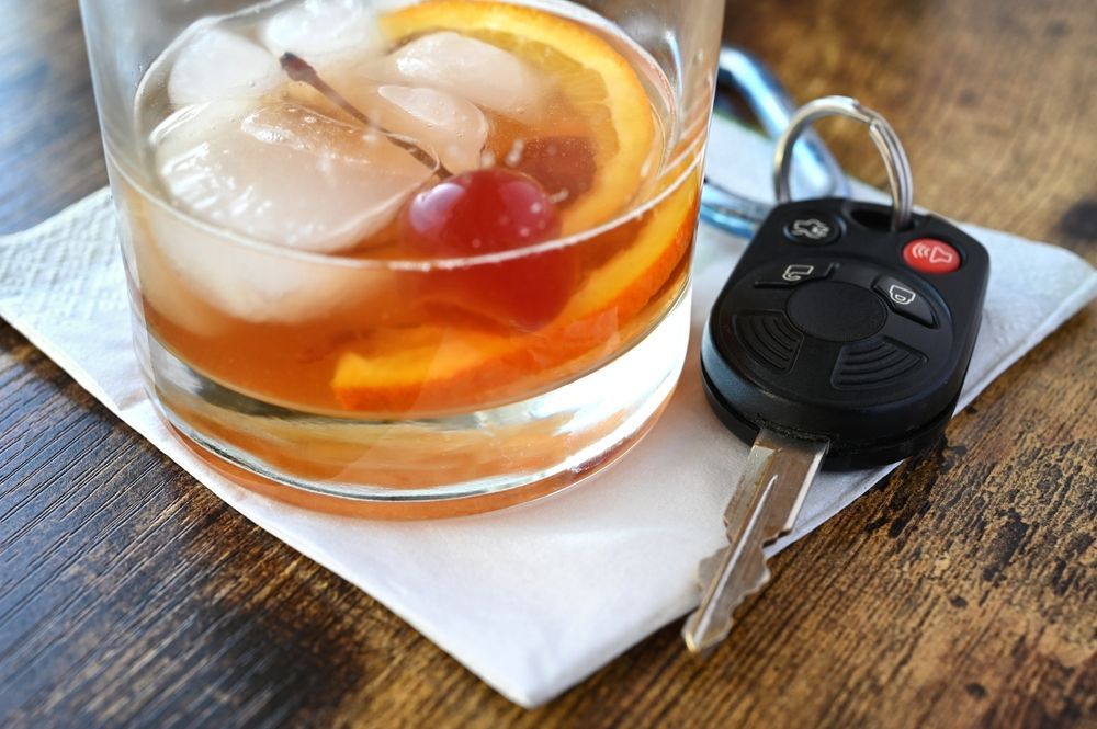 Car key beside a glass of iced tea with an orange slice on a napkin on a wooden table