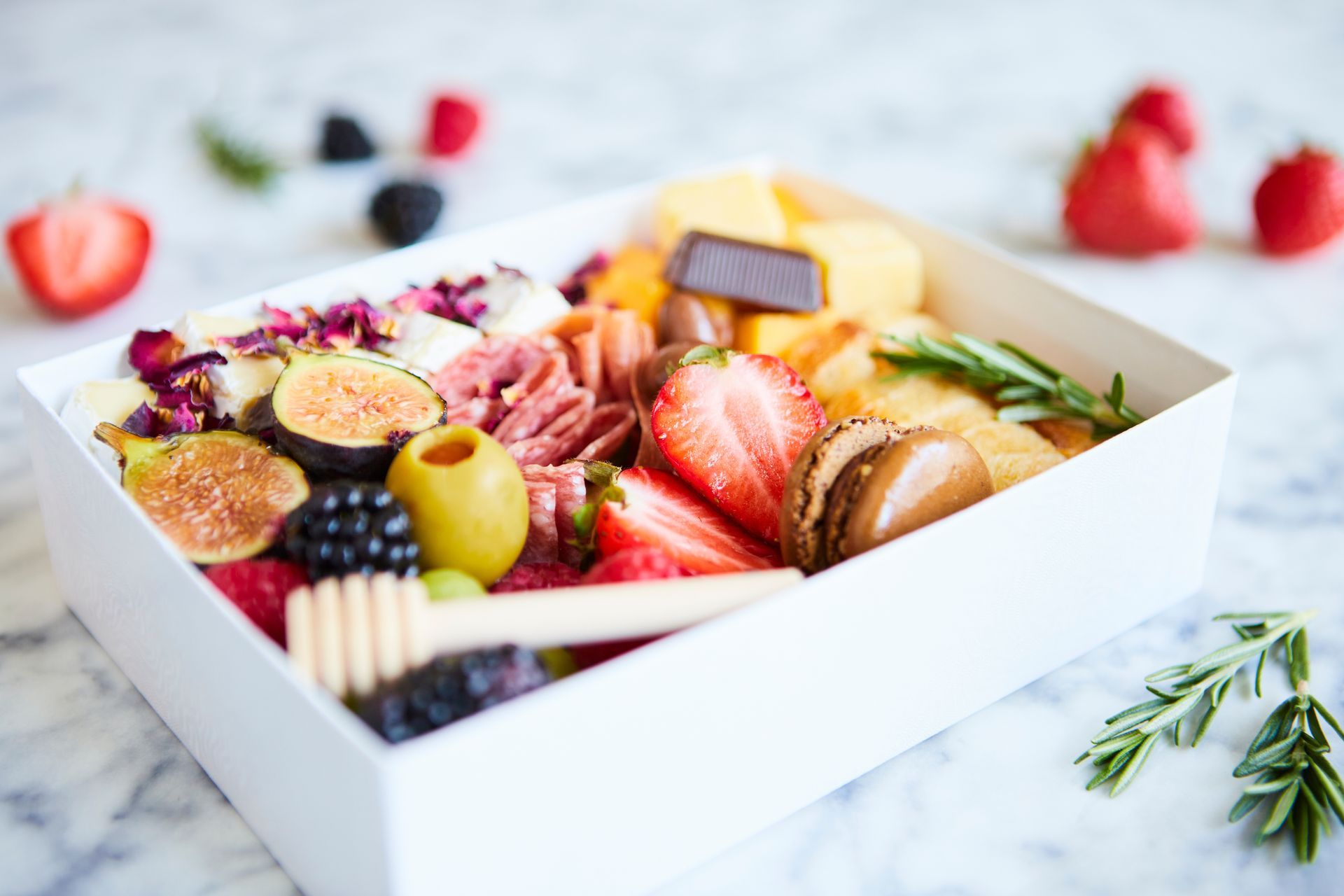 Gourmet fruit and cheese platter in a white box with strawberries, figs, grapes, nuts, and herbs