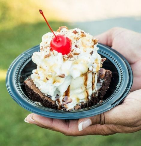 Ice cream sundae with whipped cream, cherry, and chocolate drizzle in a black bowl held in a hand