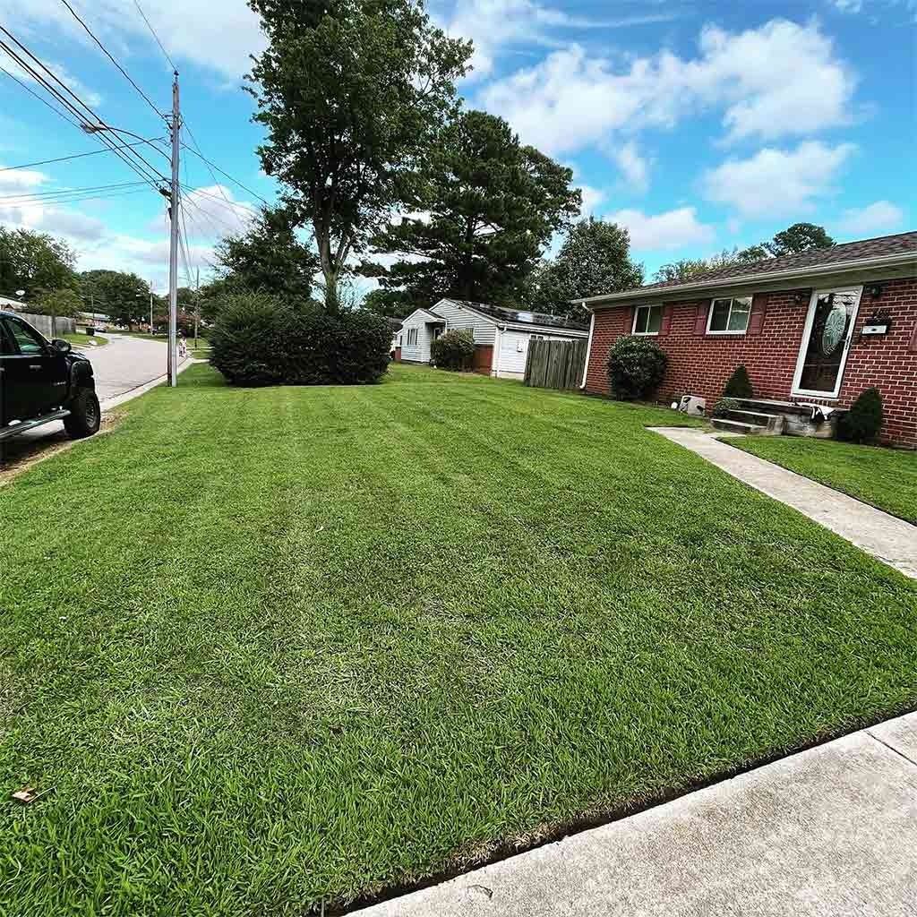 Green lawn with a house on the right, cloudy sky, and a road on the left.