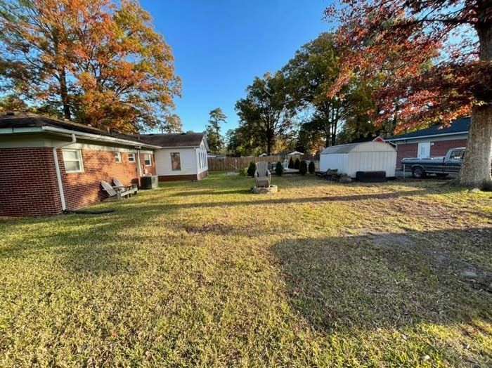 Backyard with a brick house, shed, and autumn trees under a blue sky.