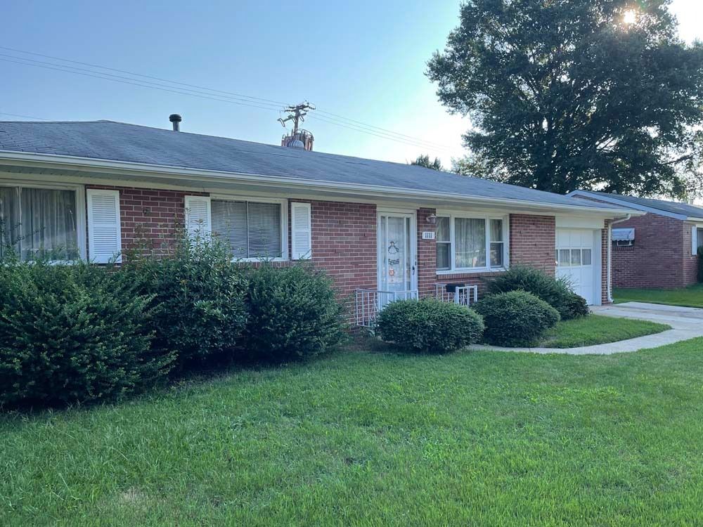 Brick ranch home with green lawn, shrubs, and attached garage.