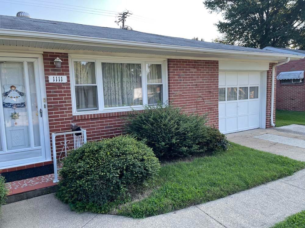 Brick house with a small lawn, bushes, and a garage. The address 